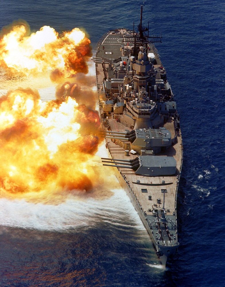 A bow view of the battleship USS IOWA (BB-61) firing its Mark 7 16-inch/50-caliber guns off the starboard side during a fire power demonstra